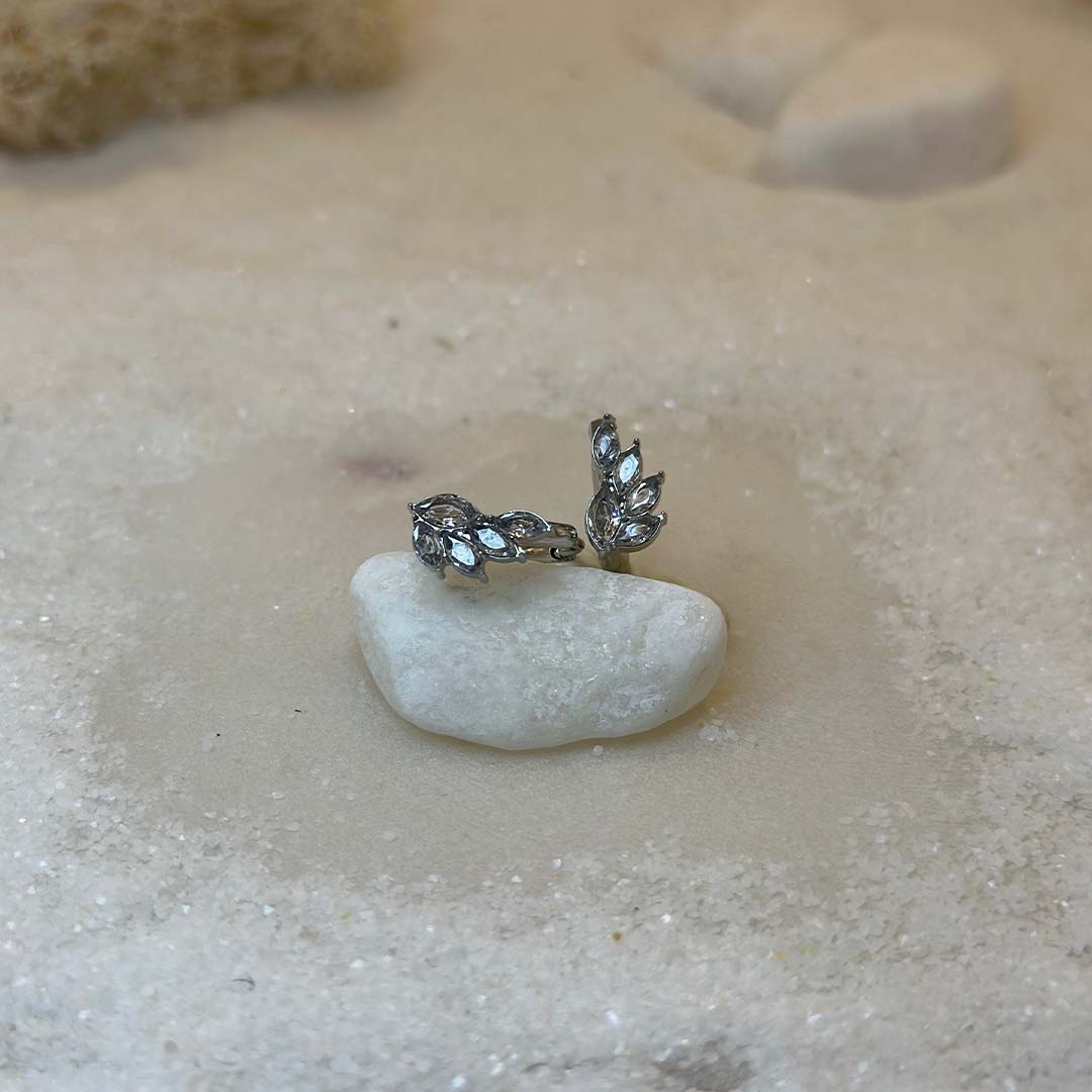 Deux très belles bagues d'argent en acier inoxydable "Ania" sont au centre de l'image, posées de face sur un caillou. Autour d'elle se trouve du sable blanc. Le fond est flou.