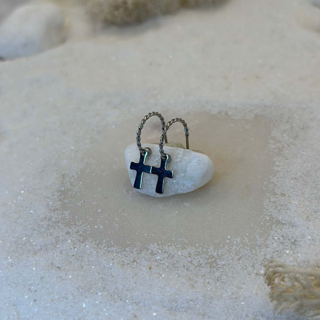 Deux magnifiques boucles d'oreilles "anna" en argent sont au centre de l'image, posées sur une caillou blanc. Ce sont des bijoux en acier inoxydable vu de 3/4. Le fond est du sable blanc.