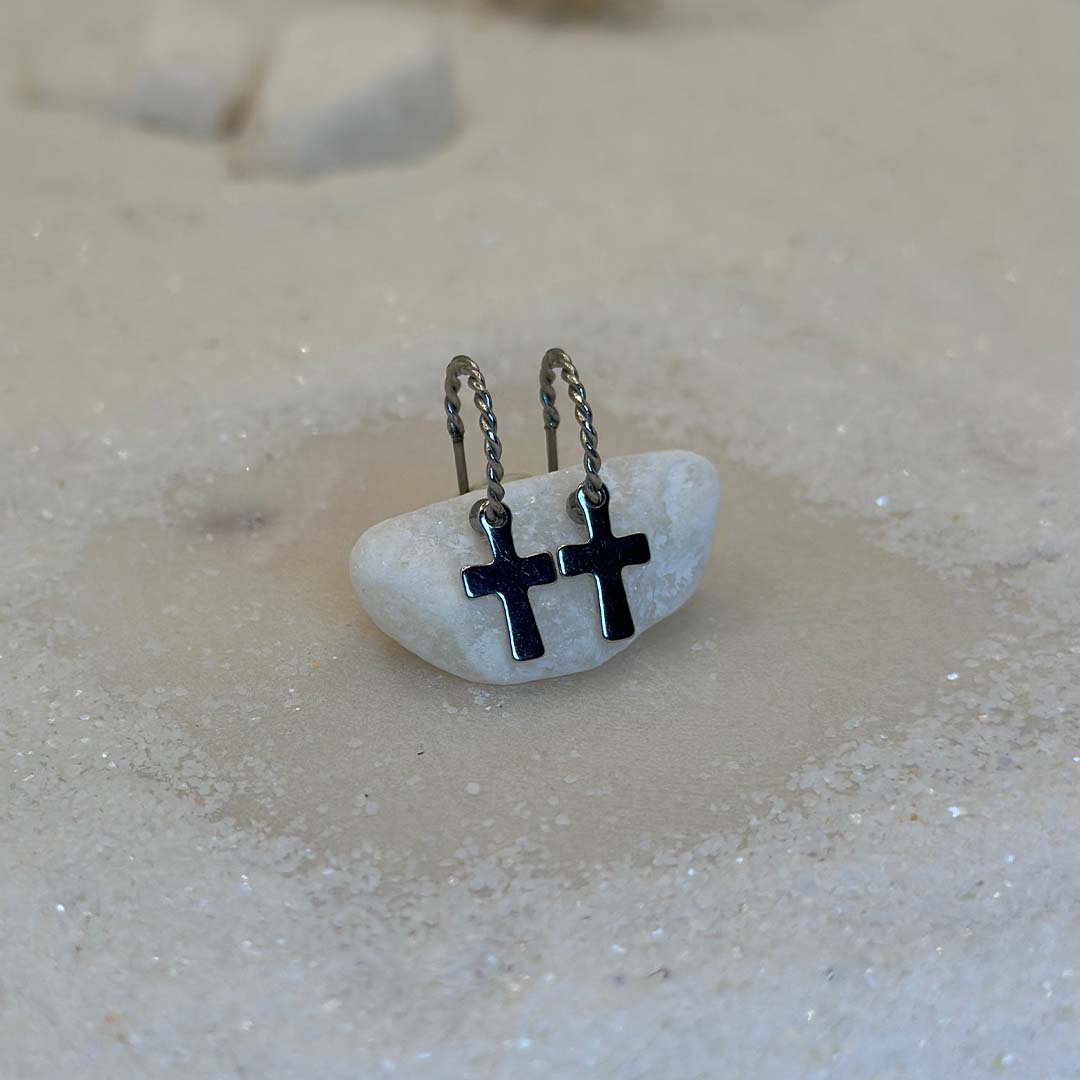 Deux magnifiques boucles d'oreilles "anna" en argent sont au centre de l'image, posées sur une caillou blanc. Ce sont des bijoux en acier inoxydable. Le fond est du sable blanc.