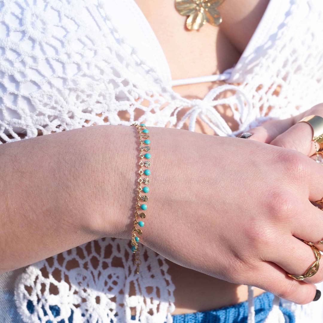Photo d'un poignet pris de près pour montrer ce magnifique bijou "ariella" en acier inoxydable qui est un bracelet avec une chaîne texturée et des jolies boules turquoises. Il est de couleur doré / or.