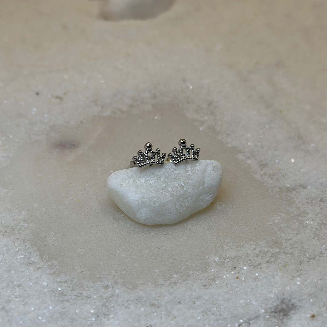 Deux très jolies boucles d'oreilles en argent "cori" sont au centre de l'image, posées sur un caillou blanc. Les bijoux en acier inoxydable sont vu de face. Autour se trouve du sable blanc.