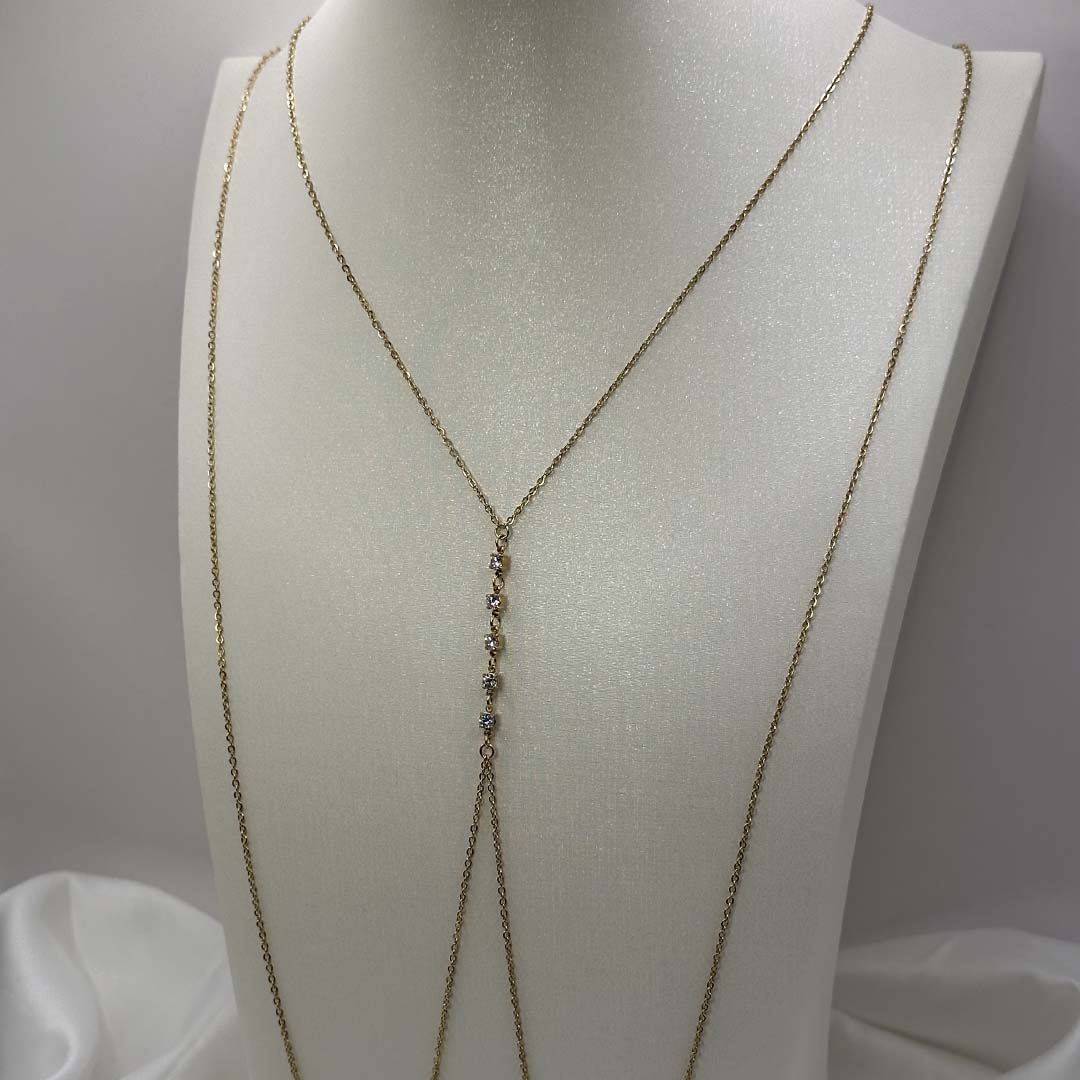 Ce magnifique bijou "Gialli" en acier inoxydable est un bijou de corps / une chaîne de buste dorée avec des strass en enfilade. Il est posé sur un buste blanc pailleté qui est sur une fond blanc et un tissu satiné blanc.