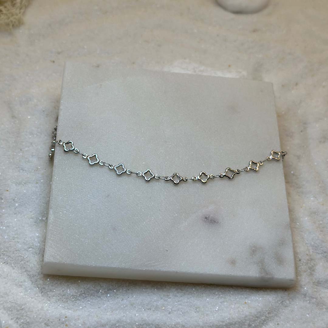 Un magnifique bracelet en argent "lori" est au centre de l'image, posé sur une plaque de marbre. Le bijoux en acier inoxydable est composé d'une chaîne en argent, ainsi que des motifs en forme d'étoiles. Autour se trouve du sable blanc.