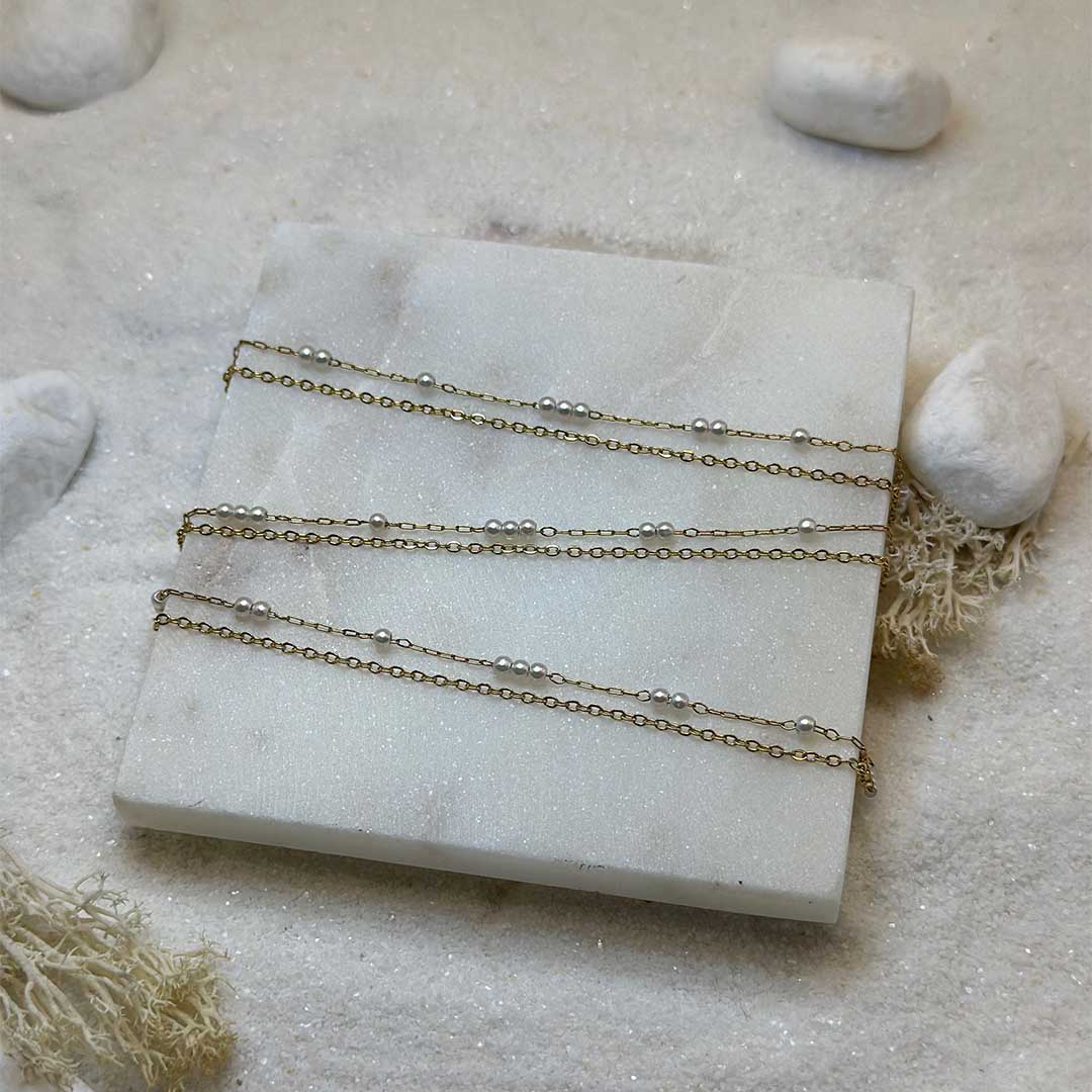 Une magnifique chaine de taille en acier inoxydable "Perla" de couleur or, ce bijou est posé sur une plaque de marbre blanche qui elle même est posé sur du sable blanc qui fait office de fond d'image.