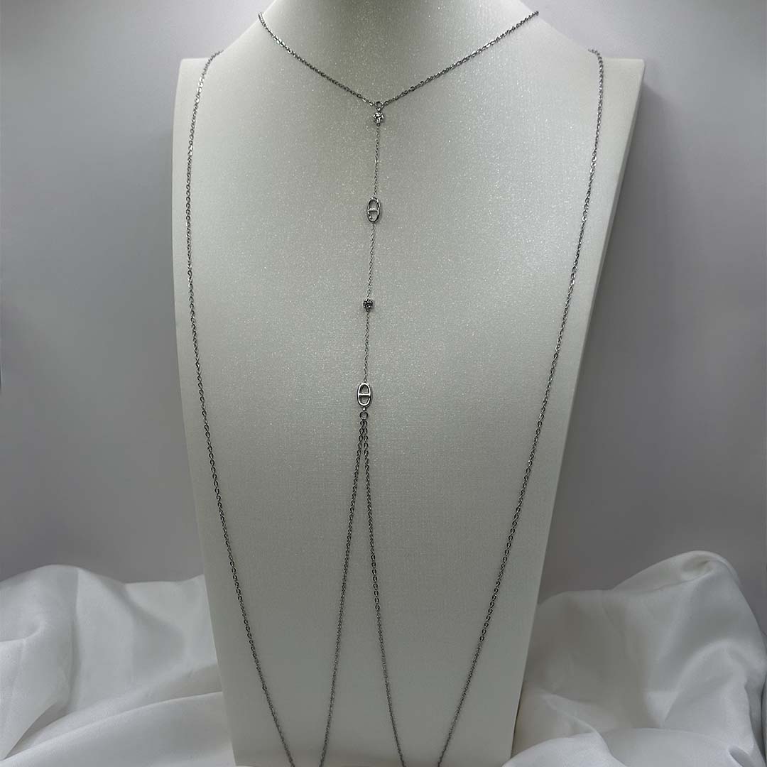 Ce magnifique bijou "Sélia" en acier inoxydable est un bijou de corps / une chaîne de buste argenté avec des strass et des charms au design de noeuds marins. Il est posé sur un buste blanc pailleté qui est sur une fond blanc et un tissu satiné blanc.