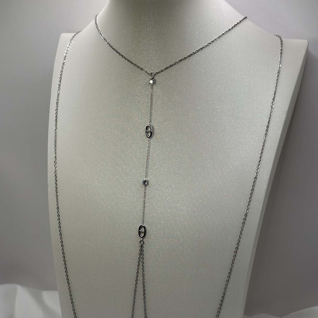 Ce magnifique bijou "Sélia" en acier inoxydable est un bijou de corps / une chaîne de buste argenté avec des strass et des charms au design de noeuds marins. Il est posé sur un buste blanc pailleté qui est sur une fond blanc et un tissu satiné blanc.