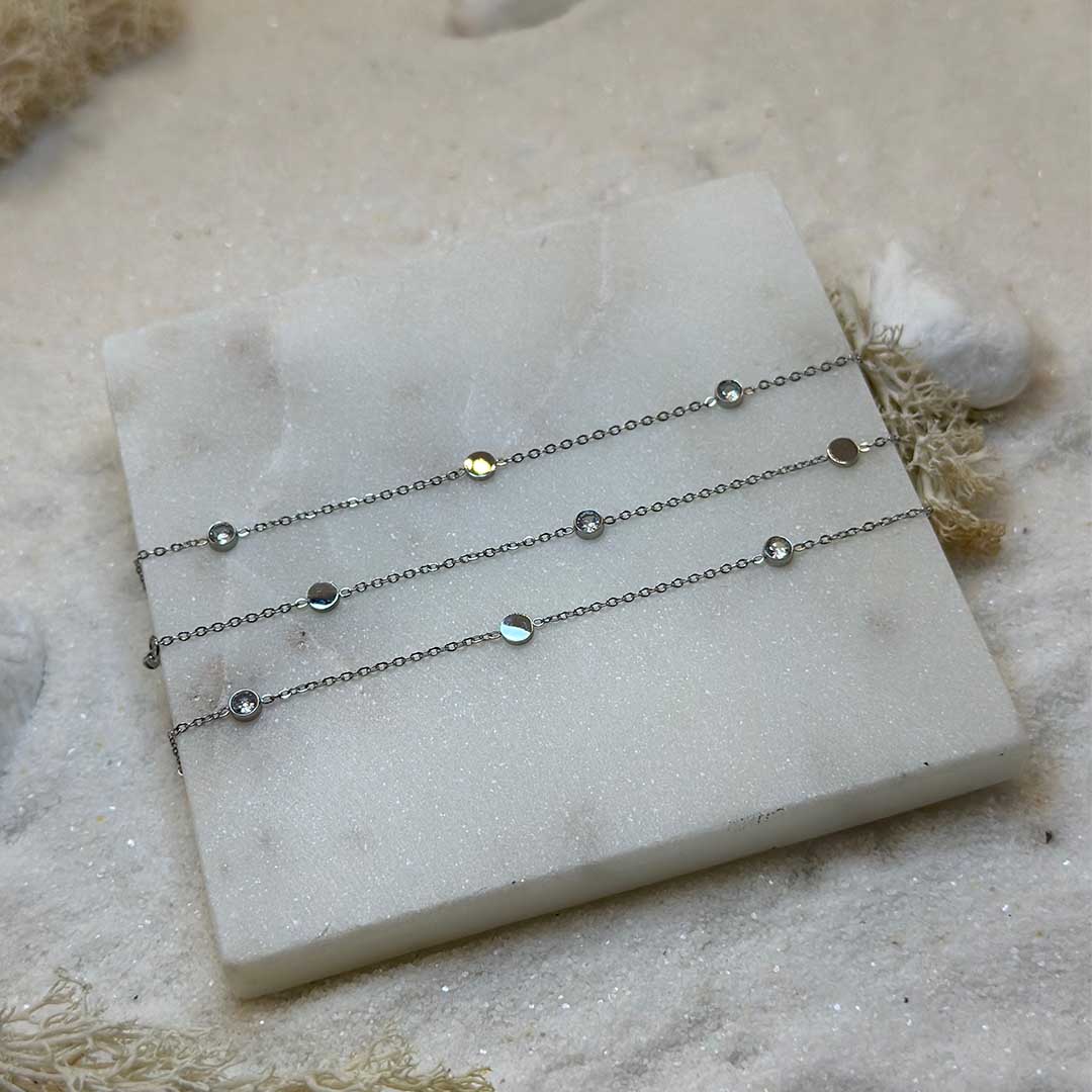 Une magnifique chaine de taille en acier inoxydable "Venicia" de couleur argent, ce bijou est posé sur une plaque de marbre blanche qui elle même est posé sur du sable blanc qui fait office de fond d'image.