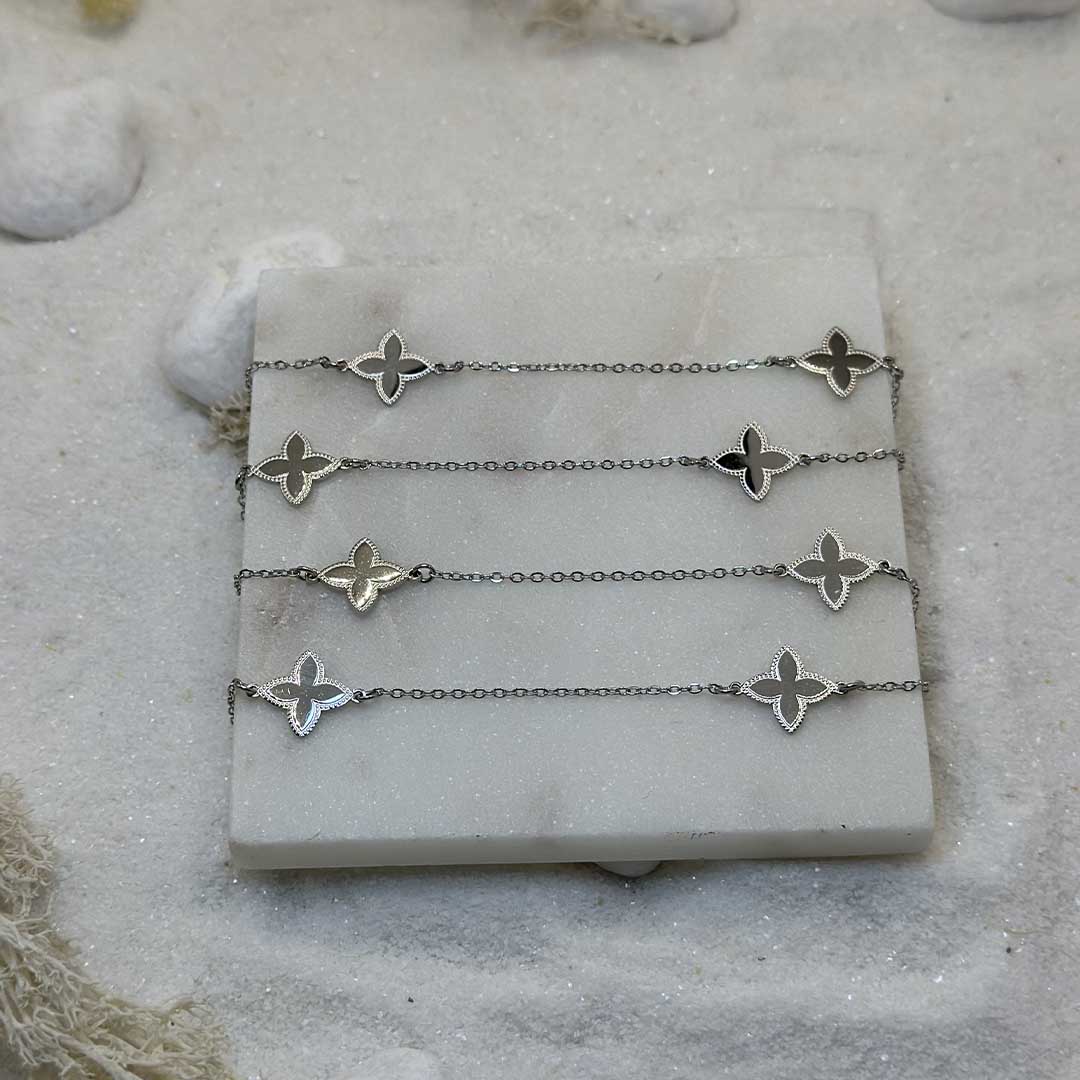 Un magnifique collier sautoir en acier inoxydable "Zelia" de couleur argent, ce bijou est posé sur une plaque de marbre blanche qui elle même est posé sur du sable blanc qui fait office de fond d'image.