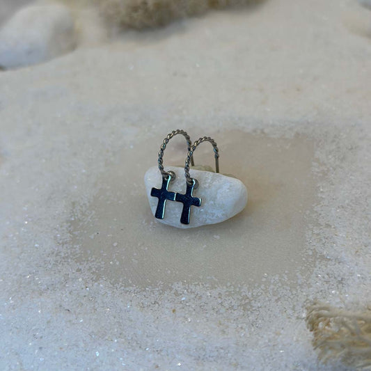 Deux magnifiques boucles d'oreilles "anna" en argent sont au centre de l'image, posées sur une caillou blanc. Ce sont des bijoux en acier inoxydable vu de 3/4. Le fond est du sable blanc.
