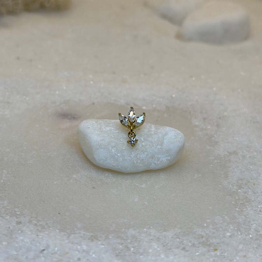 Un très beau piercing en or "diane" est au centre de l'image, posé sur un caillou blanc. Le bijoux en acier inoxydable est vu de face. Du sable blanc se trouve tout autour.