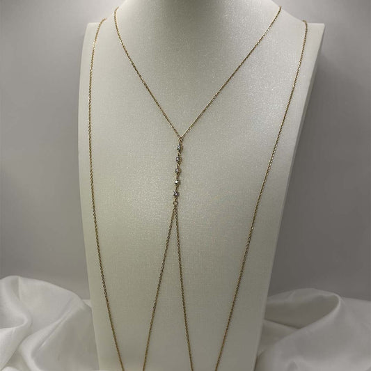 Ce magnifique bijou "Gialli" en acier inoxydable est un bijou de corps / une chaîne de buste dorée avec des strass en enfilade. Il est posé sur un buste blanc pailleté qui est sur une fond blanc et un tissu satiné blanc.