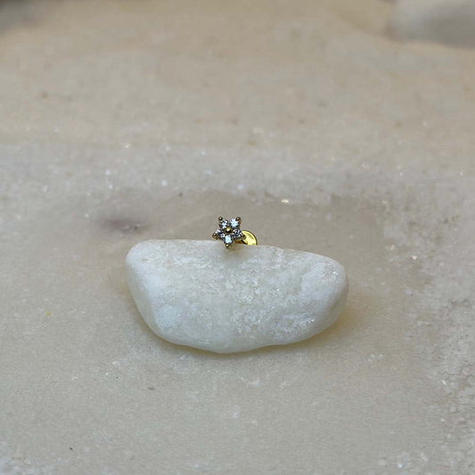 Un très beau piercing "hiny", de couleur or, est au centre de l'image. Le bijoux en acier inoxydable est posé de 3/4 sur un caillou blanc. Le fond est du sable blanc.
