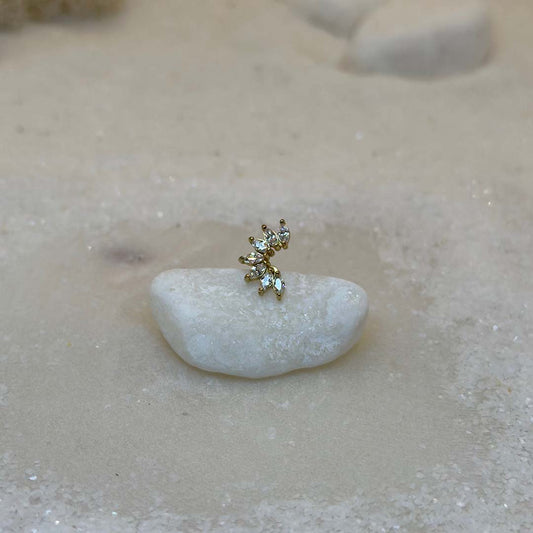 Un très beau piercing "Luisa", de couleur or, est au centre de l'image. Le bijoux en acier inoxydable est posé de 3/4 sur un caillou blanc. Le fond est du sable blanc.
