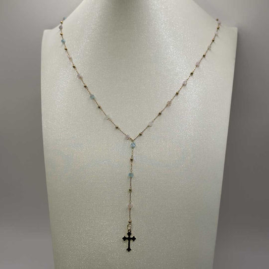 Ce joli bijou "mia" en acier inoxydable est un collier Y ou lasso avec une chaîne dorée et des pierres colorées en bleu, rose et vert. Il y a des petites boules de couleur or sur la chaîne et au bout se trouve en pendentif croix doré style gothique. Le collier est sur un buste pailleté blanc qui est devant un fond blanc.