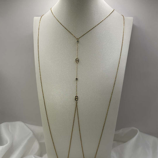 Ce magnifique bijou "Sélia" en acier inoxydable est un bijou de corps / une chaîne de buste dorée avec des strass et des charms au design de noeuds marins. Il est posé sur un buste blanc pailleté qui est sur une fond blanc et un tissu satiné blanc.