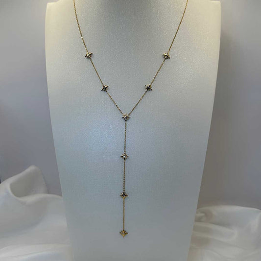 Un magnifique collier en acier inoxydable "Stary" de couleur or, ce collier est en forme Y avec plusieurs étoiles de couleur argent tout le long de ce dernier, le bijoux est posé sur un portant mannequin buste blanc avec un draps en satin blanc a la base de ce portant