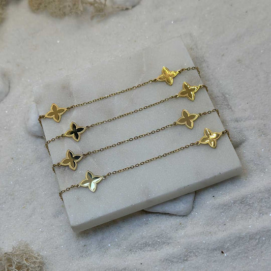Un magnifique collier sautoir en acier inoxydable "Zelia" de couleur or, ce bijou est posé sur une plaque de marbre blanche qui elle même est posé sur du sable blanc qui fait office de fond d'image.